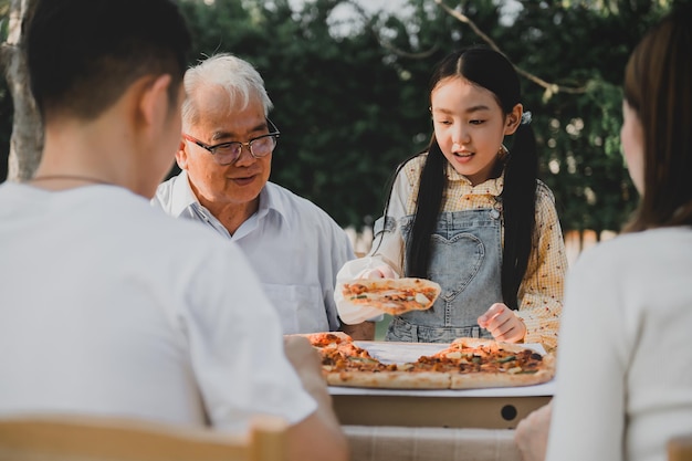 Familia asiática comiendo pizza en el jardín de casa. Padre con estilo de vida de niño y abuelo en el patio trasero.