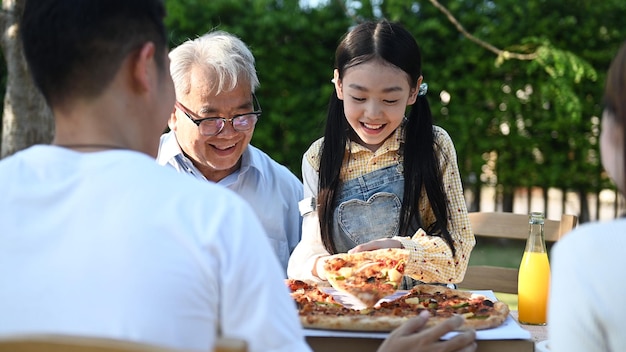 Familia asiática comiendo pizza en el jardín de casa. Padre con estilo de vida de niño y abuelo en el patio trasero.