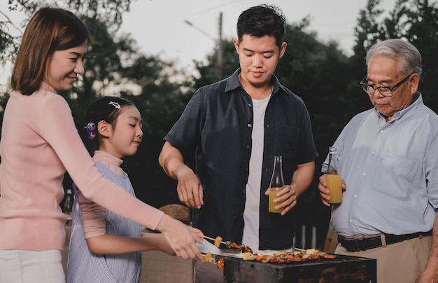 Família asiática fazendo um churrasco em casa. Cozinhando churrasco grelhado para o jantar no quintal. Estilo de vida nas férias de verão.