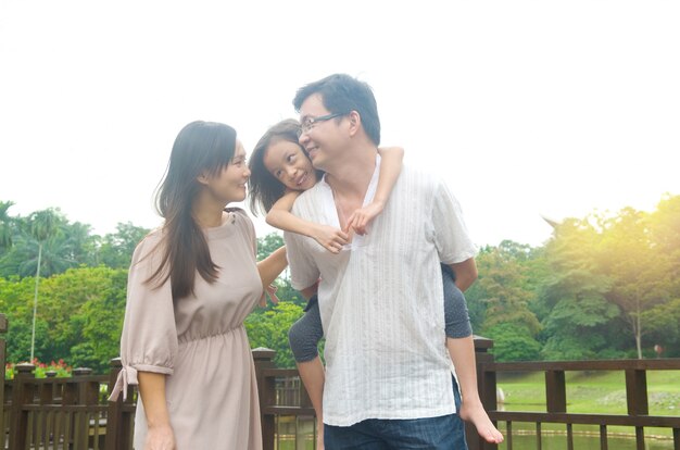 Família asiática feliz ao ar livre. Pai, piggybacking, filha, andar, jardim, parque, esposa