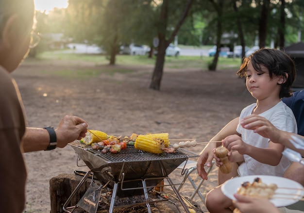 Familia asiática feliz haciendo barbacoa juntos. Cocinar barbacoa a la parrilla para cenar durante el campamento en la playa de verano.