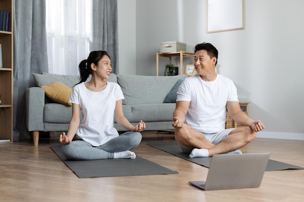 Familia asiática feliz haciendo yoga matutino en casa usando una computadora portátil