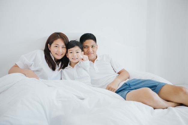 Familia asiática feliz con el hijo en casa en el dormitorio jugando y riendo