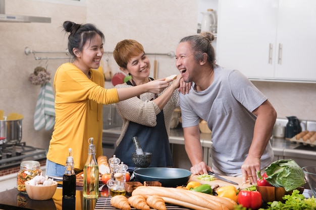 Familia asiática feliz de madre padre e hija cocinando en la cocina haciendo comida sana juntos sintiéndose divertido