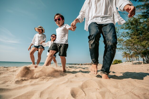 Família asiática feliz Os pais estão de mãos dadas com os filhos e caminhando na praia nas férias