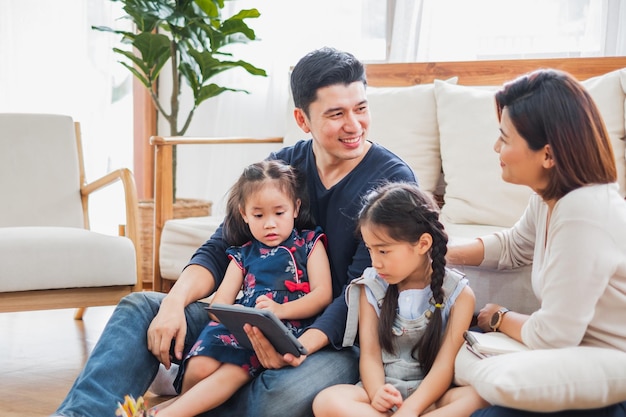 Familia asiática feliz usando una tableta portátil para jugar viendo películas relajándose en casa por concepto de estilo de vida