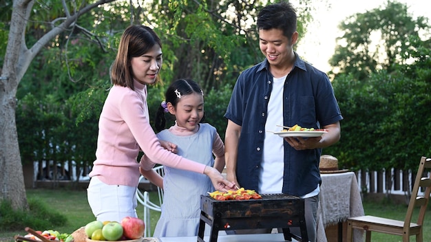 Familia asiática haciendo una barbacoa en casa. Cocinar barbacoa a la parrilla para cenar en el patio trasero. Estilo de vida en vacaciones de verano.