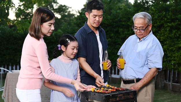 Familia asiática haciendo una barbacoa en casa. Cocinar barbacoa a la parrilla para cenar en el patio trasero. Estilo de vida en vacaciones de verano.