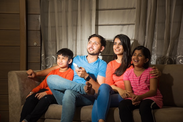 Familia asiática india de cuatro viendo la televisión o la televisión mientras está sentado en el sofá o el sofá