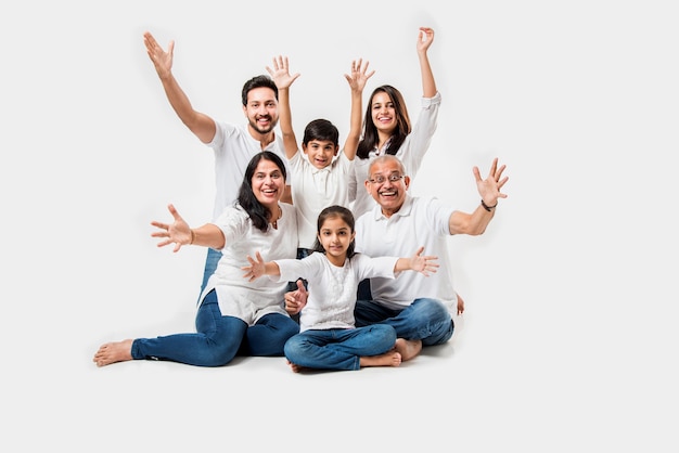 Familia asiática india que se sienta sobre el fondo blanco. pareja de ancianos y jóvenes con niños vistiendo pantalones vaqueros azules y top blanco. enfoque selectivo