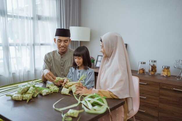 Família asiática muçulmana fazendo ketupat para eid mubarak juntos