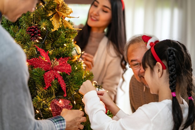 Familia asiática multigeneracional decorando un árbol de Navidad.