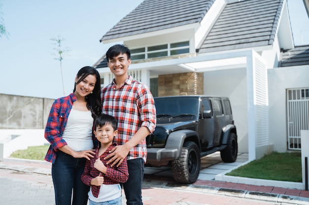 Familia asiática con niño delante de su casa y coche