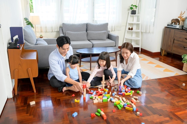 Familia asiática con niños jugando y construyendo una torre de coloridos bloques de juguete de madera en la sala de estar