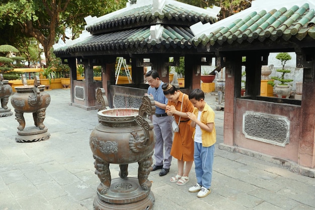Família asiática orando durante a visita ao templo