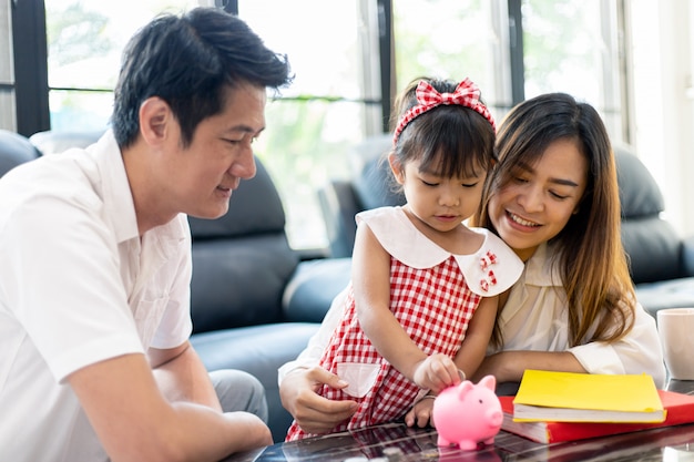 Familia asiática poniendo dinero en la hucha para ahorrar