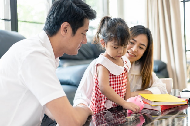 Familia asiática poniendo dinero en la hucha para ahorrar