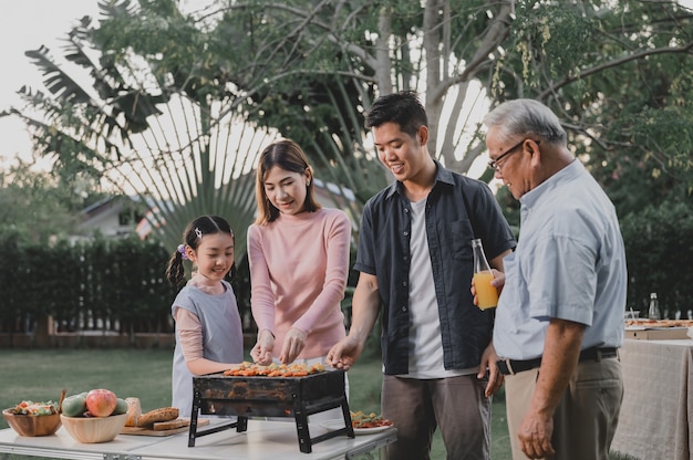 Familia asiática que tiene una fiesta de barbacoa en casa. Cocinar barbacoa a la parrilla para cenar en el patio trasero. Estilo de vida en vacaciones de verano.