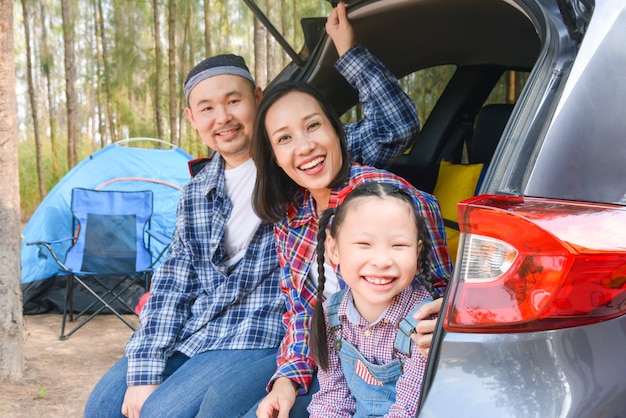 Familia asiática sentada en el maletero del coche yendo de campamento de vacaciones. Viaje familiar en coche.