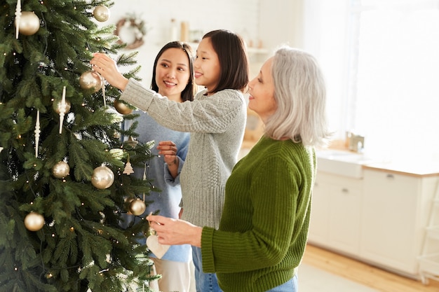 Familia asiática de tres decorando el árbol de Navidad juntos preparándose para la víspera de Navidad en casa