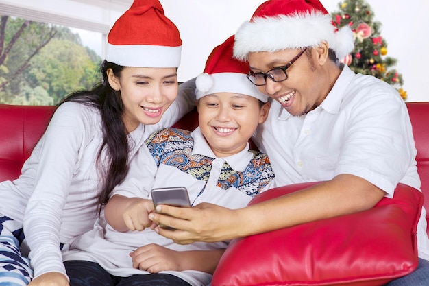 Familia asiática usando un teléfono inteligente cerca del árbol de Navidad