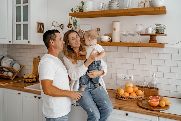 una familia con un bebé en jeans y camisetas blancas está jugando en la cocina