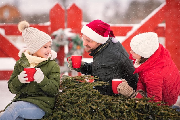 Família bebendo chá para se aquecer em um trenó com árvore de Natal em um inverno nevado lá fora