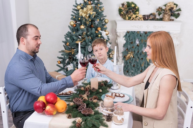 Familia bebiendo vino sentado en una mesa con el telón de fondo del árbol de Navidad