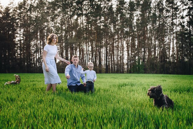 Familia en el bosque en un picnic. Sentarse en un claro, hierba verde. Ropa azul Mamá y papá juegan con su hijo, se abrazan y sonríen. Un niño con gafas. Tiempo juntos Canasta de picnic con comida. Perro mascota.