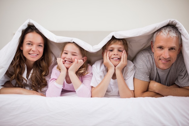 Família brincalhão deitada sob um edredon