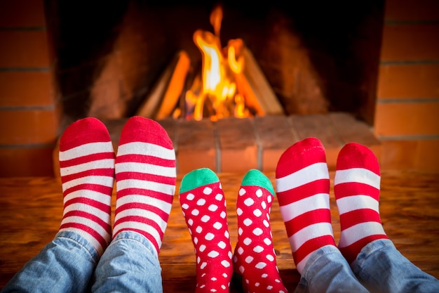 Familia en calcetines de Navidad junto a la chimenea. Mamá; padre y bebé se divierten juntos. Gente descansando en casa