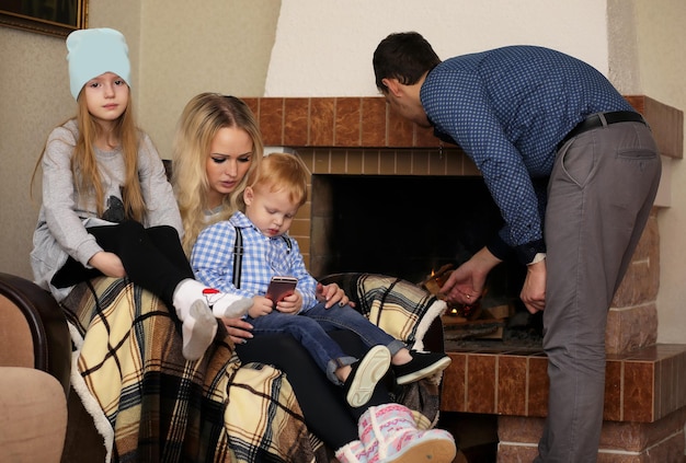 Foto familia calentada por la chimenea sentada en el sofá en casa