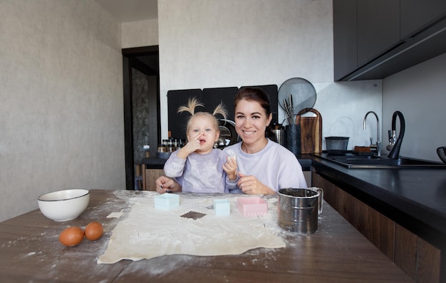 Familia cariñosa feliz cocinando panadería juntos. Madre e hija cocinan galletas y se divierten en la cocina. Comida casera y un pequeño ayudante.