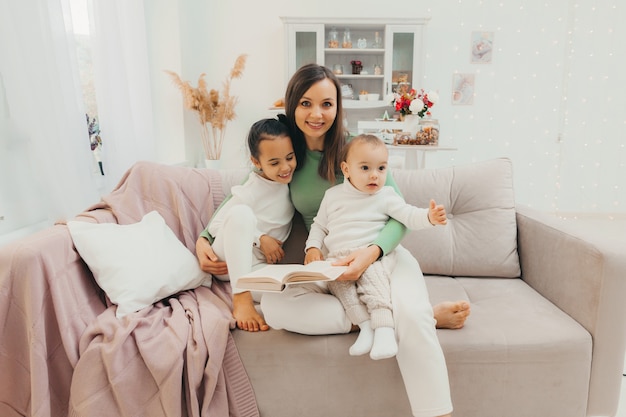 Familia cariñosa feliz. hermosa joven mamá lee un libro a sus hijos en el sofá de la sala de estar.