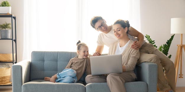 Familia cariñosa feliz. Joven madre, padre e hija usando laptop. Mamá divertida, papá y un niño encantador se divierten en casa.