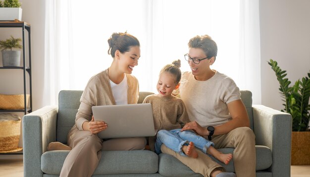 Familia cariñosa feliz. Joven madre, padre e hija usando laptop. Mamá divertida, papá y un niño encantador se divierten en casa.