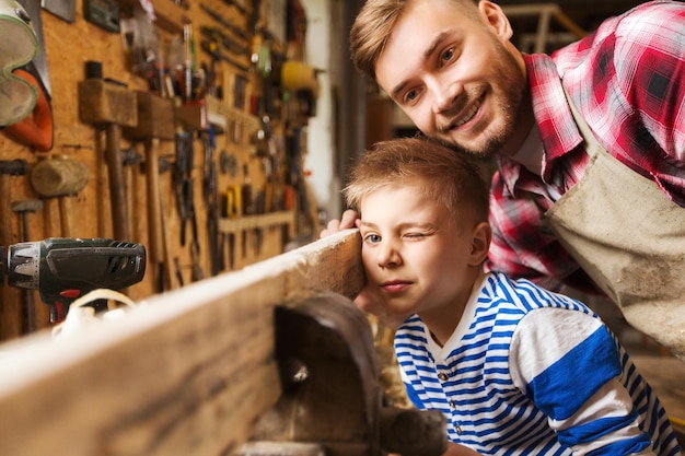 Família, carpintaria, carpintaria e conceito de pessoas - pai e filho pequeno testando a uniformidade da prancha de madeira na oficina