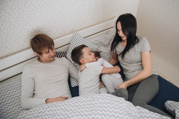 Familia en casa en pijama. Hija e hijo. Levantarse en la mañana. Abrazándose y besándose en el dormitorio sobre la cama.