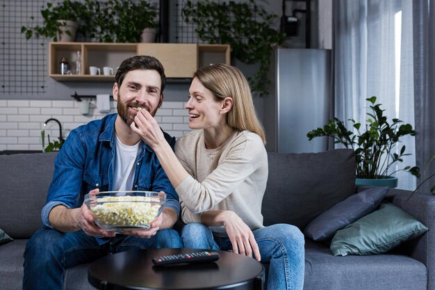 Família casal feliz homem e mulher comendo pipoca e assistindo tv sentado no sofá em casa