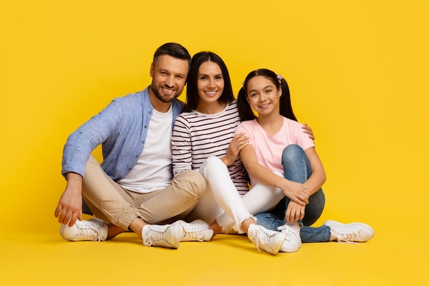 Família caucasiana feliz de três pessoas sentadas no chão e abraçadas