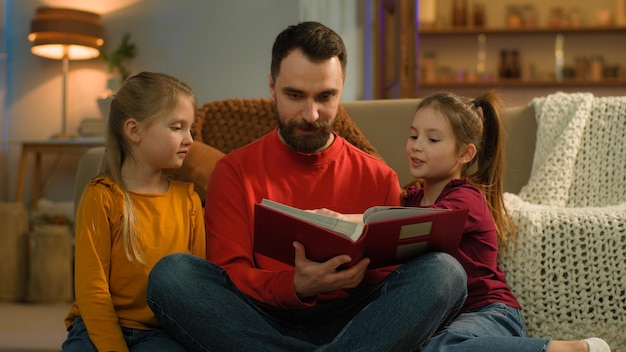 Família caucasiana tarde da noite à noite em casa pai pai pai homem lendo livro crianças vendo foto