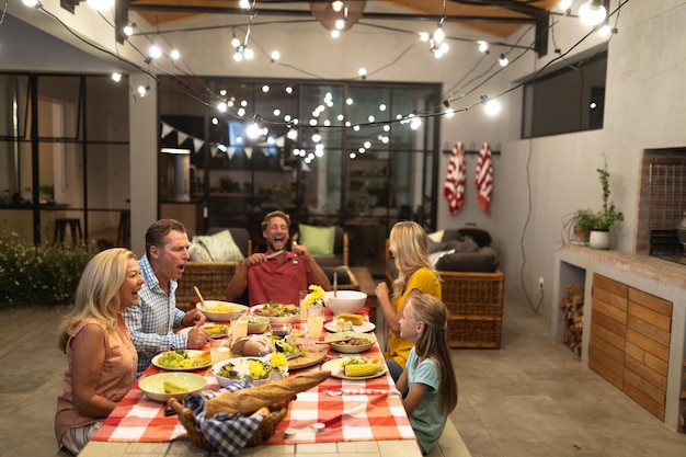 Familia caucásica multigeneracional disfrutando juntos de su tiempo en casa, sentados junto a una mesa, poniendo comida en sus platos, comiendo juntos