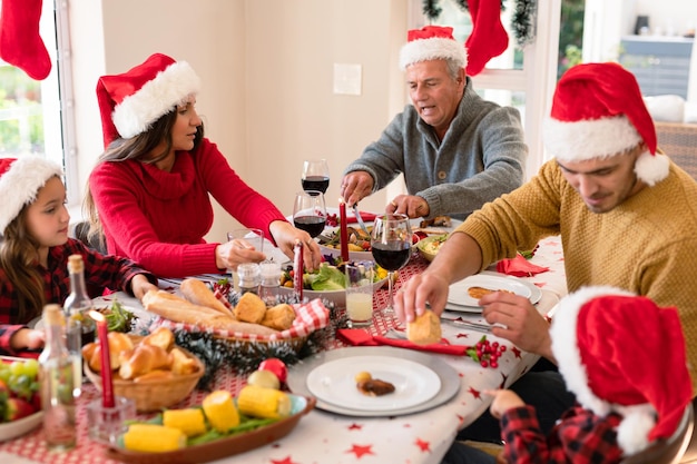 Familia caucásica de varias generaciones con sombreros de Papá Noel comiendo Navidad. Navidad familiar y festividad juntos en casa.