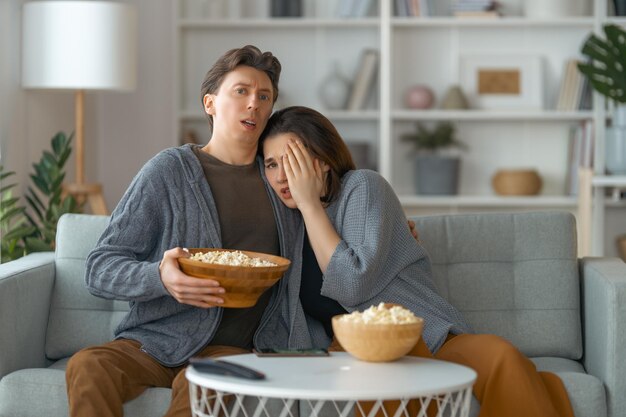 Família chocada com pipoca sentada no sofá e assistindo TV em casa Casal passando tempo juntos