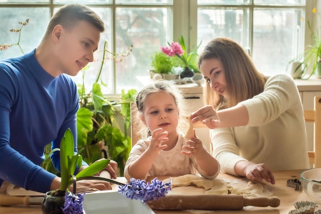 Familia cocina en casa mamá papá e hija amasan la masa en una cocina hombre niña mujer juntos