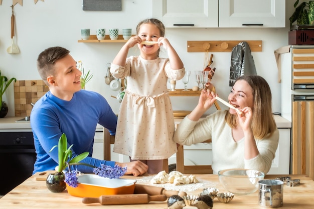 Familia cocina en casa mamá papá e hija amasan la masa en una cocina hombre niña mujer juntos