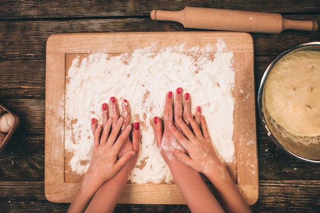 Familia cocinando pasteles caseros, las manos de la madre y la hija en harina sobre una mesa.