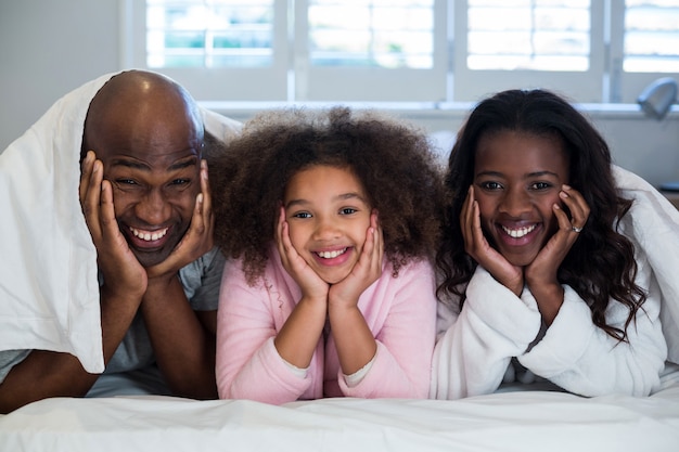 Família com as mãos no rosto, deitada na cama