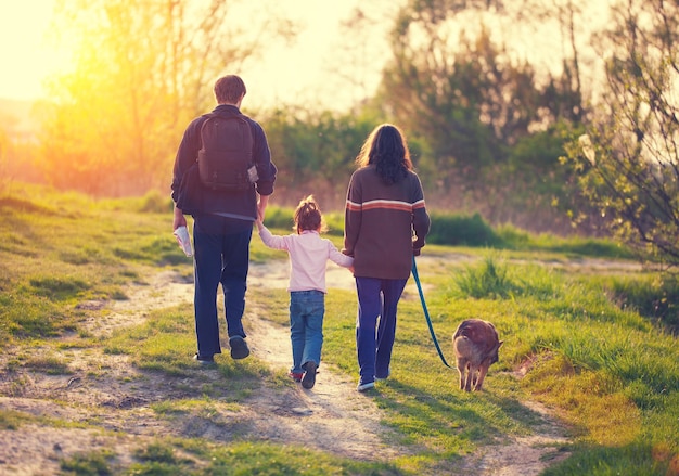 Foto família com cachorro andando na vila ao pôr do sol de volta à câmera