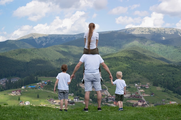 Família com dois filhos fica em uma colina, olhando para as montanhas.